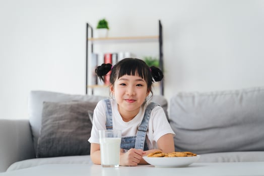 A young girl is sitting on a couch with a glass of milk and a plate of cookies. photo