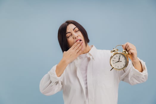 Sleepy woman yawning and holding alarm clock in studio photo