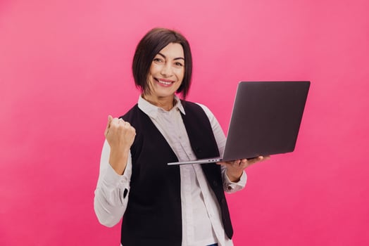 Excited brunette businesswoman celebrating success holding laptop on pink background photo