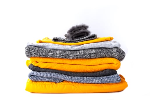 Pile of clothes. Warm yellow and grey sweaters and jumpers in stack on white background. photo