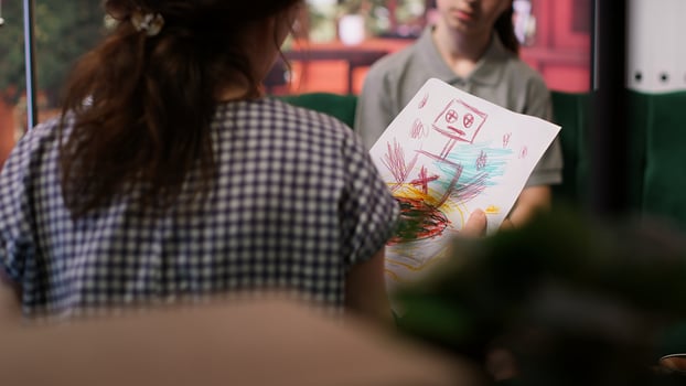 Teenager showing dark gory sketches that reveal anxiety and warning signs, violent thoughts during a therapy session. Psychologist analyzes disturbing art, searching for signs of hostility. Camera A. photo