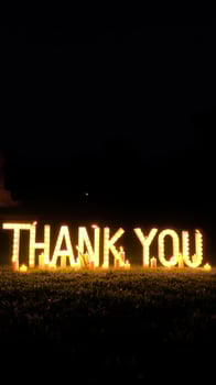 Lighted thank you sign displays gratitude during a night gathering in an outdoor celebration photo