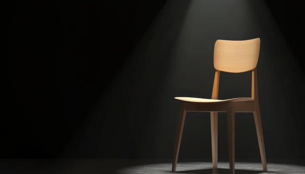 A lone wooden chair sits illuminated in darkness photo