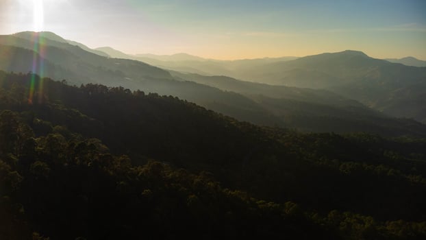 Beautiful sunset in the winter. The setting sun shines down on a serene mountain landscape covered with tropical trees in the evening. photo