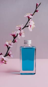 Rectangular glass bottle of blue liquid, with delicate pink blossoms on pastel pink surface. Vertical Mobile Wallpaper photo