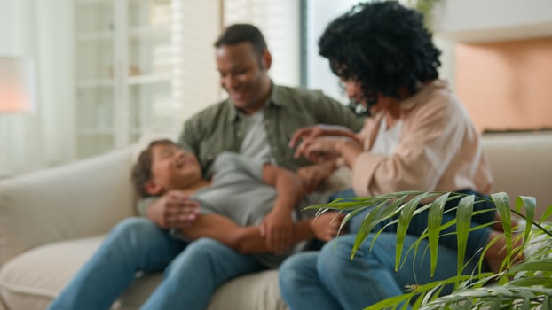 Bonding family African American parents with little adopted kid boy son tickling on home sofa playing together sincere laugh having fun happy childhood adorable playful child boy kidding with mum dad photo