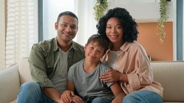 Multiracial African American Caucasian happy family portrait at home smiling parents father and mother hug little boy child preschool kid on sofa couch diverse generation parenthood love children care photo