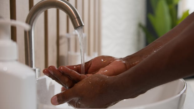 Close up African American man washing dirty hands with soap warm water in hotel bath toilet using hand sanitizer hygiene wash care rinsing palms in sink bathroom coronavirus protection body skincare photo