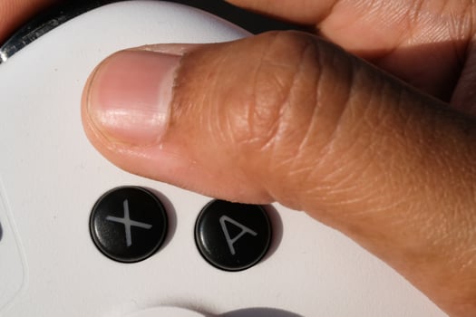 Thumbs are pressing buttons on a white gamepad. The game controller buttons are set soft and ergonomic. Finger mechanics and gameplay. Hobbies and leisures. Macrophotography Theme photo