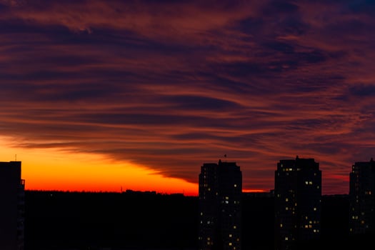 Vibrant sunset over a silhouetted city skyline. Colorful clouds paint the sky with warm hues, contrasting against the urban landscape photo