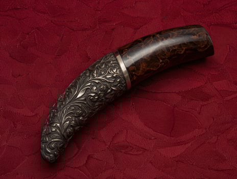 Ornate silver handle on a curved dark brown knife photo