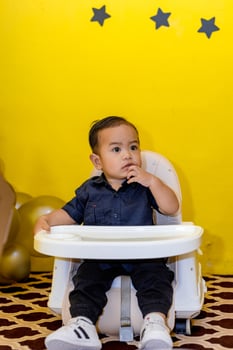 Cute adorable baby boy sitting in his high chair. Cute toddler Biting His Finger in a Sweet Pose. photo
