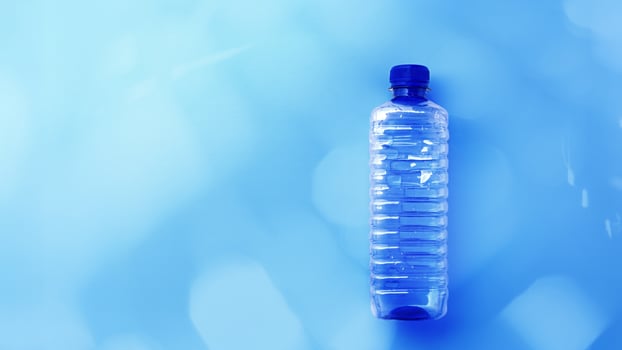 Clear plastic water bottle on bright blue background with light reflections, color gradient banner with copy space. Minimal style top view photo, one transparent blue bottle, overview flat lay photo