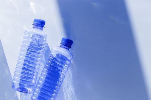 Blue plastic water bottles on white blue background with sunlight shadow and sun flare, Minimal top view photo, themes of ecology, recycling, sustainable living, reduce disposable plastics photo