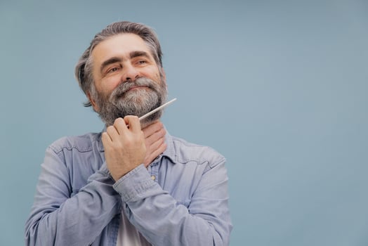 Pensive Senior Man Grooming his Beard with a Comb on Blue Background photo