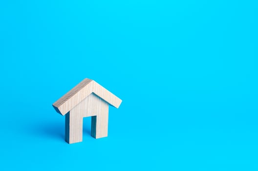 Wooden figurine of a residential building on a blue background. Minimalism. Mortgage loan. Affordable housing. Rent or sale real estate. Construction industry. Realtor services. Copy space. photo
