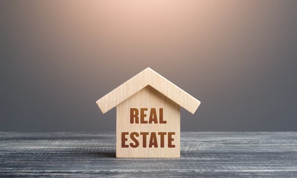 Wooden figurine of a house with word Real Estate. Buying and selling. Housing, realtor services. Construction industry, building maintenance. Mortgage loan. Assets and tax payments. Stamp duty photo
