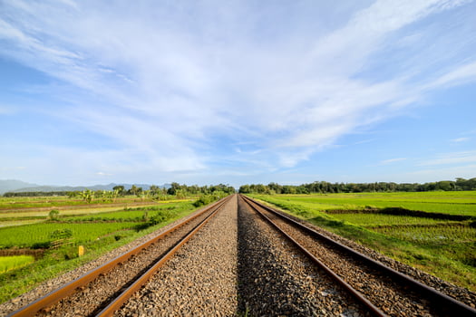 Railway Tracks Across Green Rice Fields on a Sunny Morning. Two-Way Railway Lines Through Rice Fields Under Clear Skies. Serene Morning View of Railway Tracks and Rice Paddies photo