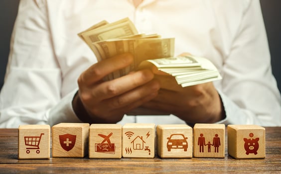 A man counts money and blocks with the attributes of family needs. Family budget concept, bills expenses, vacation and transportation. Optimal salary, sustain an acceptable standard of living. photo