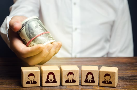 A man holds out money dollars over blocks with employees. Fair pay increase. Incentives for employees with bonuses. Investments. Company personnel costs maintenance. Payday. Salaried workers. photo