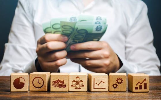 A man is counting money and blocks with business attributes. Good business model. Profitability. The rules for successful investment. High performance, great work. Company management photo