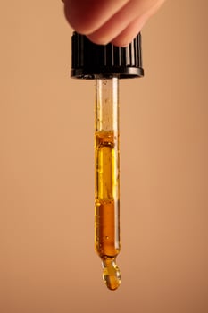The hand is holding a pipette from which drops of yellow oil are dripping photo
