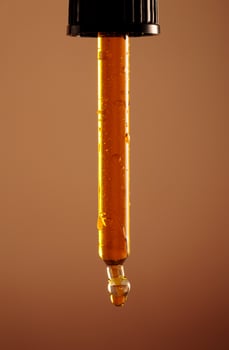 yellow oil pouring out of a pipette on a dark brown background photo