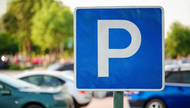 Blue metal city street parking sign, blurred cars in background. Urban car park space, traffic photo