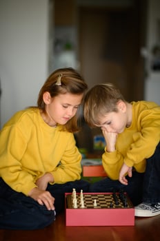 One child makes a move in chess, sitting across from an opponent in a yellow sweater. photo