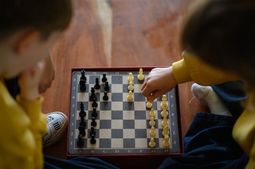 Two kids in yellow sweaters sit quietly, concentrating on a tense chess match. photo