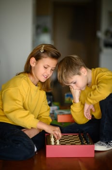 Children in yellow sweaters share a moment of laughter while deciding their chess strategies. photo