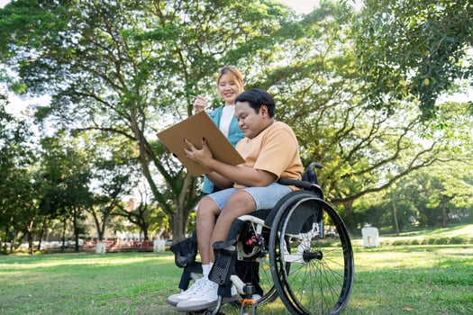 Disabled artist creating artwork with encouragement from instructor in a sunny park setting photo