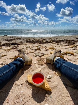 A person is relaxing while laying on the warm beach, holding a cup filled with a vibrant red liquid that catches the sunlight beautifully, enjoying the serene coastal view photo