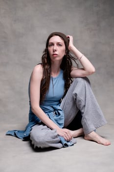 beautiful and long-haired woman in a hat and stylish clothes poses in a photo studio with a serious face.