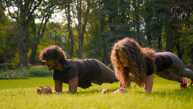 Healthy practice sport strong multiracial couple Arabian Indian man fitness trainer training with Caucasian woman pair workout in nature park doing plank position exercise on grass challenge together photo