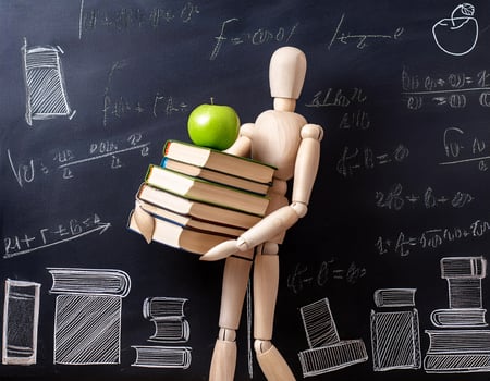 Wooden Figurine Holding a Fresh Green Apple with Book Piles and Green Chalkboard Behind photo