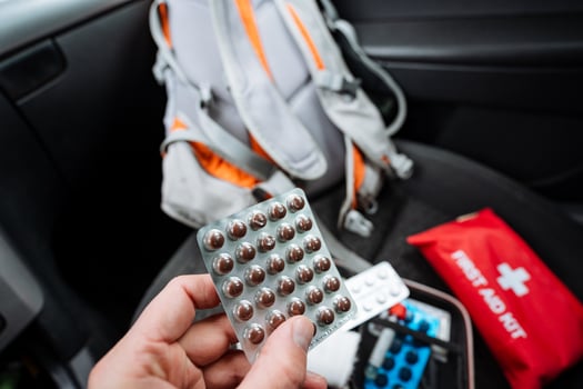 An individual is currently holding a blister pack that contains pills right in front of a wellequipped first aid kit, indicating a situation that may require medical attention photo