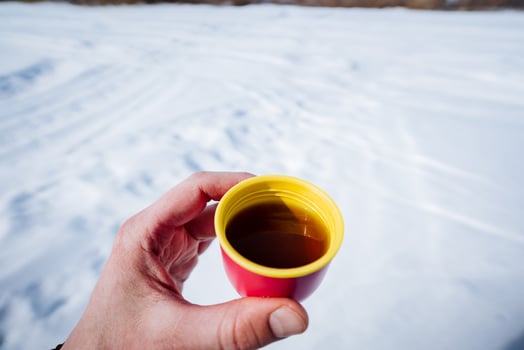 Person sipping Kopi tubruk from a cup in the snow while wearing eyewear photo