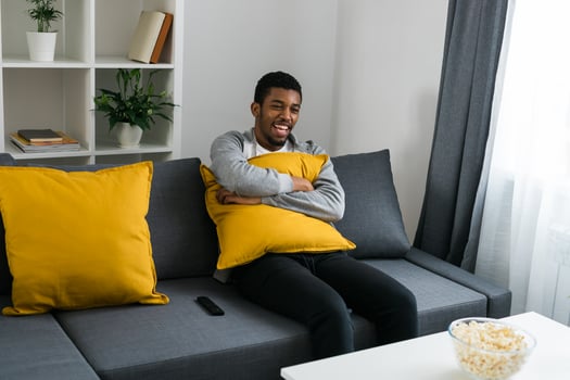 Cheerful curly haired ethnic african american male in casual clothes resting at home on comfortable sofa while watching tv channels or movie during weekend. Tv set, online television and entertiment photo