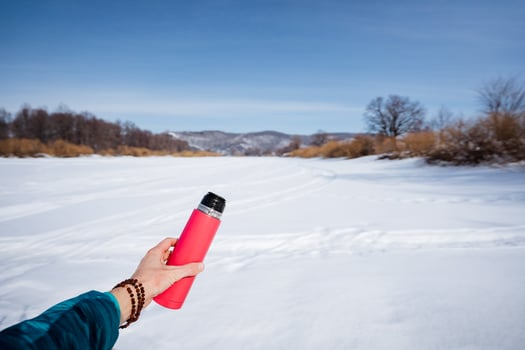 A person holding a red and pink water bottle in the snow photo