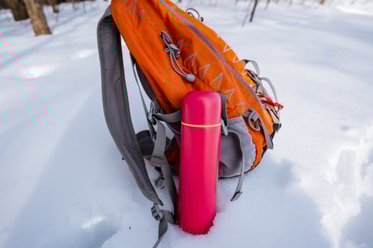A backpack with a pink water bottle sitting in the snow photo