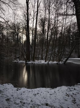 Tranquil winter scene capturing a snowy pond reflecting the setting sun through bare trees in a prague forest Vinor Nature Reserve photo
