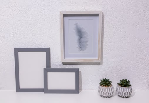 Stylish minimalist decor in light colors on a white table in a modern space. Two gray photo frames, a painting, pots. Front view. eco items.
