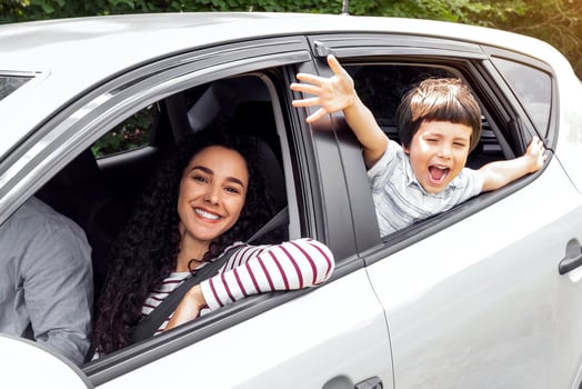 Glad young arabic man and woman driving car, little excited boy with open mouth gesturing, waving with hands at window, outdoor in summer. Weekend, auto trip with family, road and vacation together photo