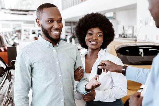 Salesman giving car key to young black couple at auto dealership. African American clients buying or renting automobile at showroom. Vehicle local distribution concept photo