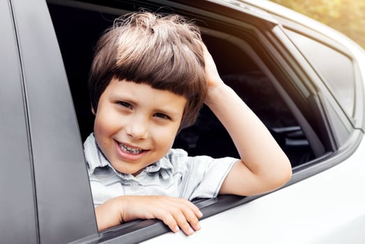 Cheerful caucasian small kid go on vacation by car and looks out window, enjoys trip and weekend, outdoor, close up. Family journey on new car together, safety in auto and life insurance, copy space photo