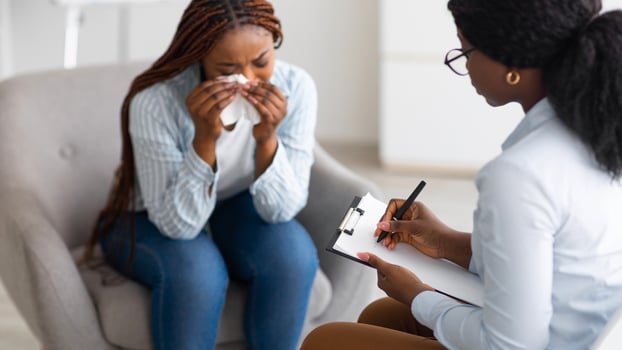 Unhappy black young woman crying at psychologist's office, panorama. Depressed millennial lady consulting psychiatrist, having session with counselor, dealing with negative emotions at clinic photo