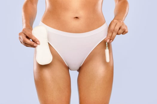 Female Period and Intimate Hygiene. Closeup cropped view of young woman in white panties holding tampon vs clean menstrual pad near hips standing isolated on blue studio background, banner photo