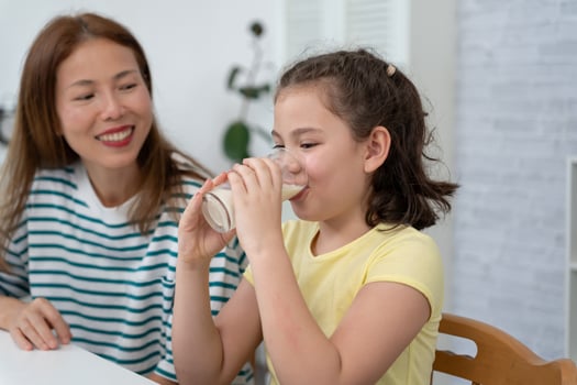 young little girl learn at home. Do homework with kind mother help, encourage for exam. Mom pass on a glass of milk to daughter. Girl happy Homeschool. Mom teach and advice education together. photo