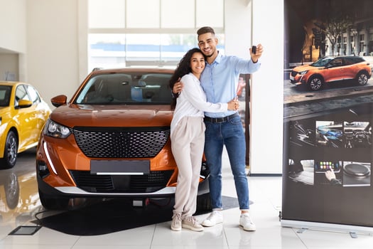 Happy middle eastern couple young man and woman standing by nice brand new car, holding key, embracing and smiling, buying new auto together at luxury showroom, panorama with copy space photo
